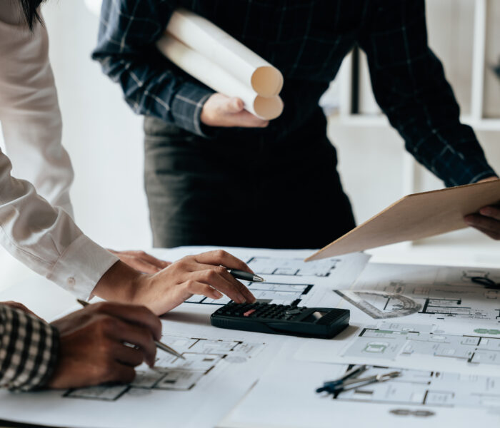 Close up of hands working brainstorming and measuring for cost estimating on paperworks and floor plan drawings about design architectural and engineering for houses and buildings.
